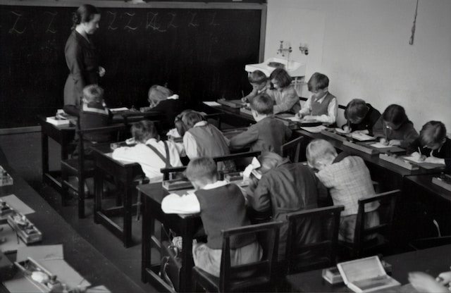 A black and white photo of a classroom with children sitting at desks.