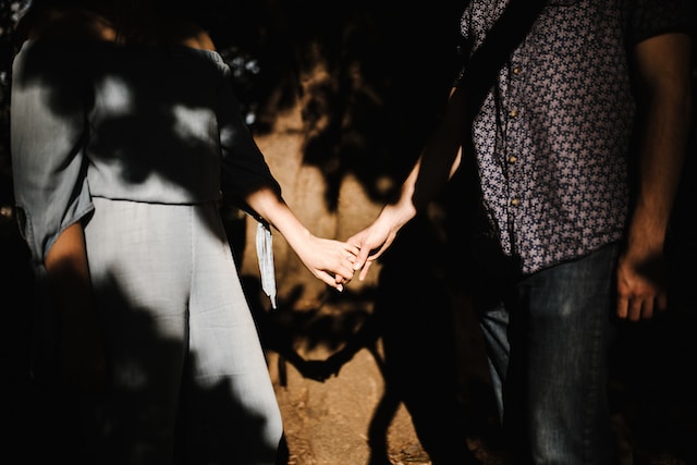 A couple holding hands in the shadow of a tree.